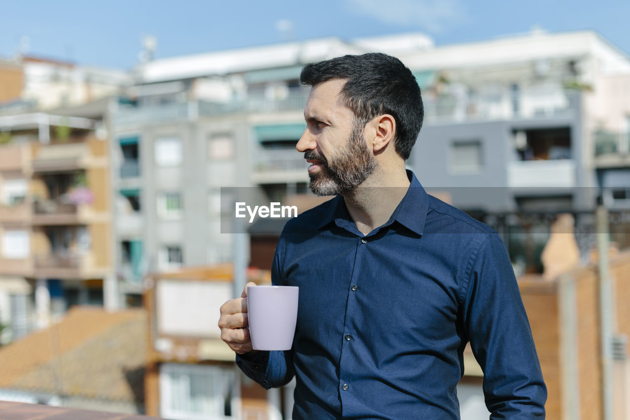 Relaxing moment of a middle-aged man standing on the balcony drinking coffee