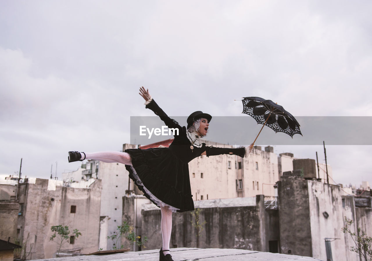 Woman holding umbrella while standing with arms outstretched on terrace