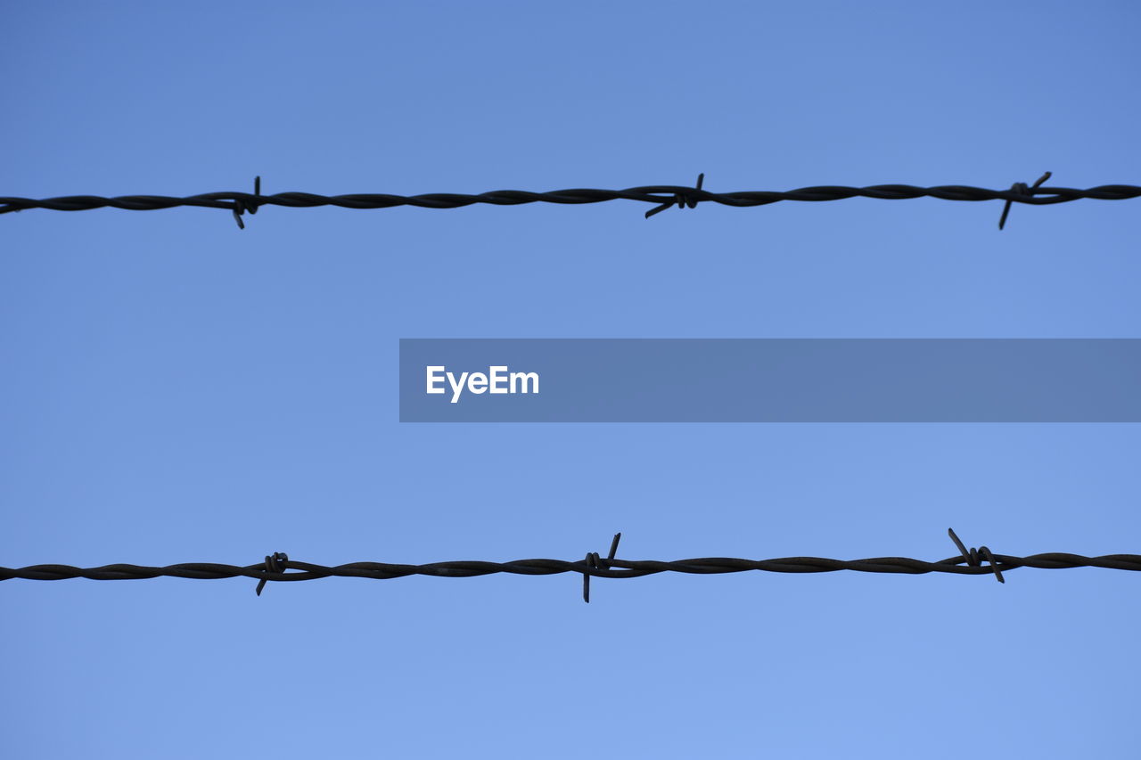 CLOSE-UP OF BARBED WIRE AGAINST CLEAR SKY