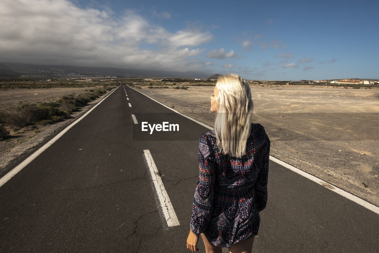 REAR VIEW OF WOMAN STANDING ON ROAD