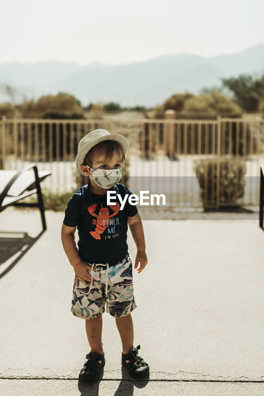 Young toddler boy with mask on standing by pool in palm springs