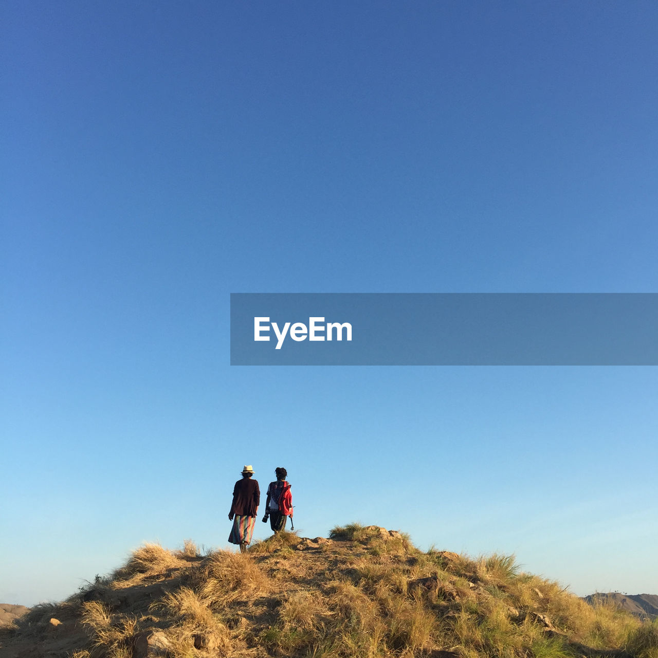 Rear view of people walking on mountain against clear blue sky