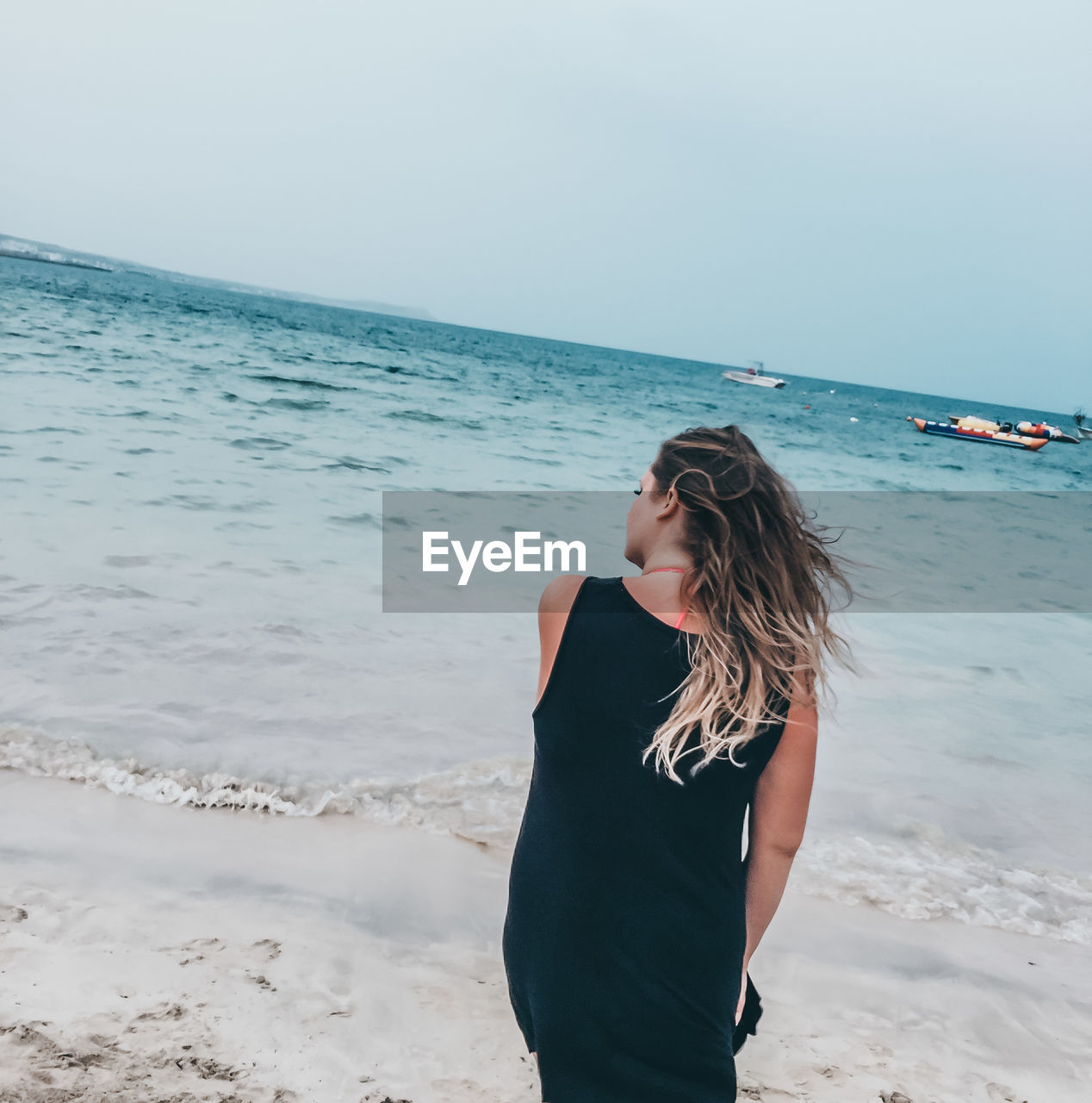 YOUNG WOMAN STANDING ON BEACH AGAINST SEA