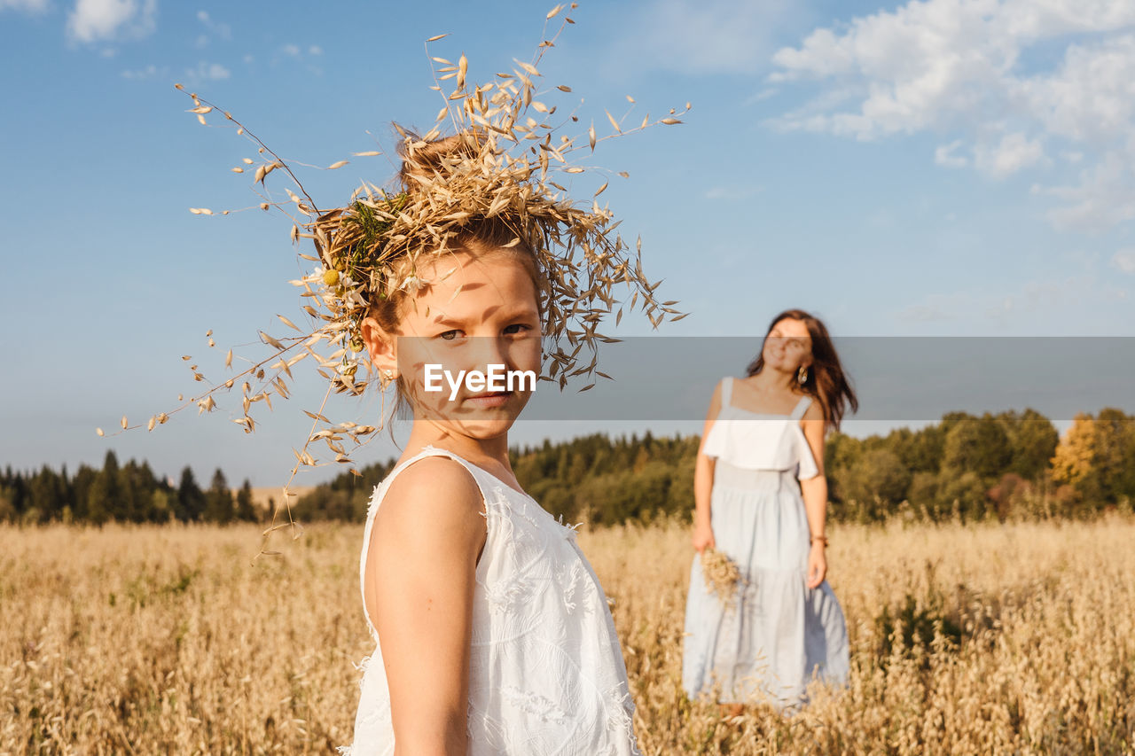 Portrait of girl wearing plants on head with mother in background