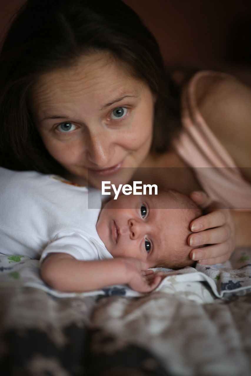 Portrait of smiling boy lying on bed at home with mother 