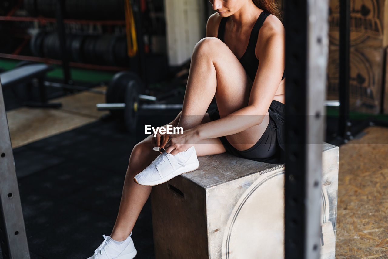 Athlete wearing sports shoe while sitting on box at gym