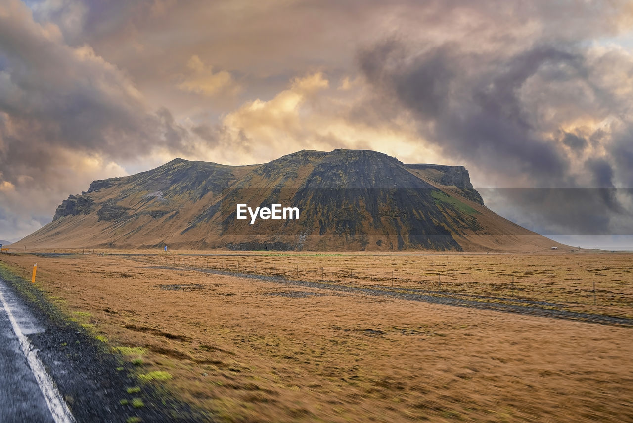 Scenic view of mountain by road in valley against dramatic sky during sunset