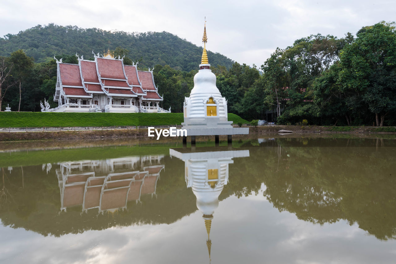 Reflection of buddhist stupa on lake at a temple in thailand against sky