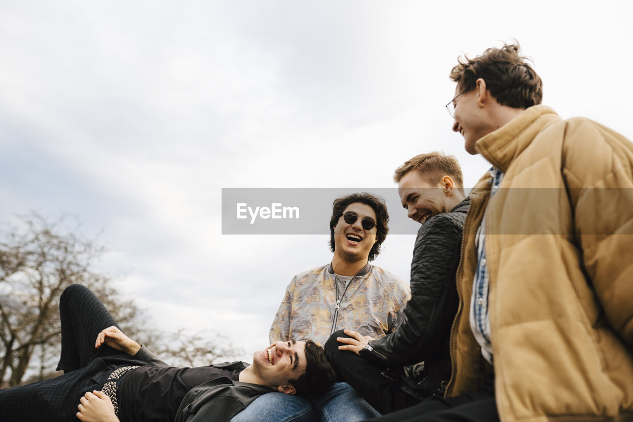 Cheerful male friends spending leisure time against sky