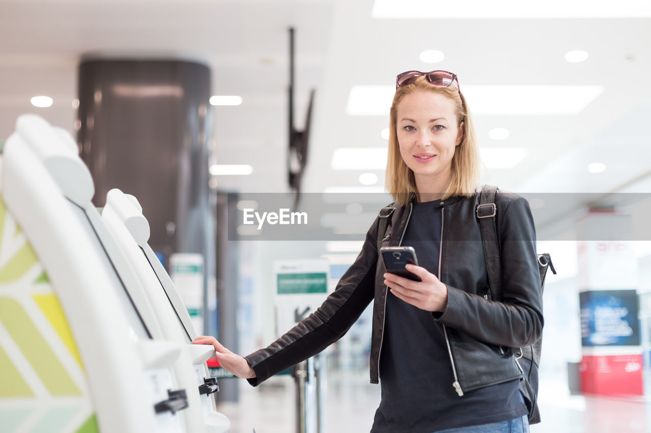 Portrait of smiling woman holding smart phone while standing at airport