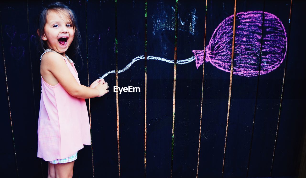 Optical illusion of happy cute girl holding balloon drawn on wooden wall