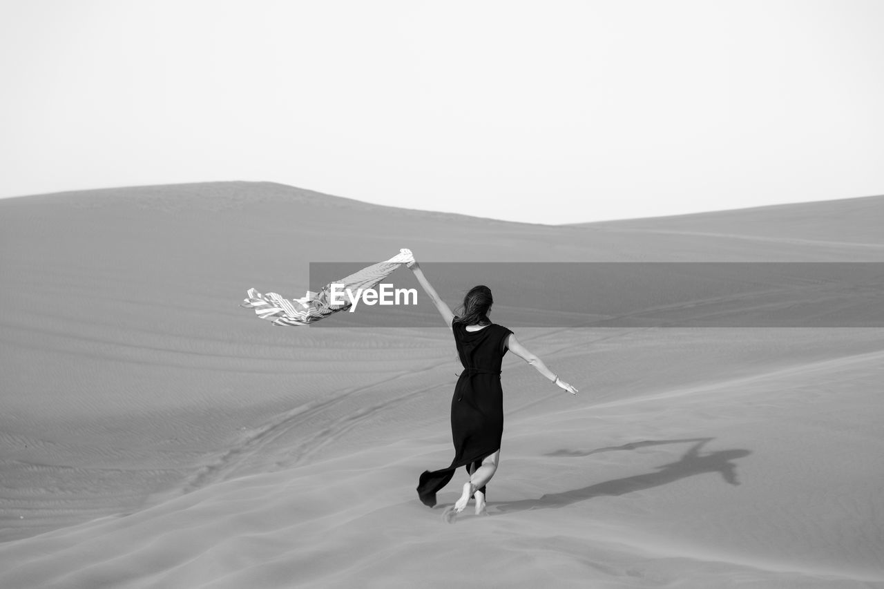 Rear view of woman walking at desert against clear sky