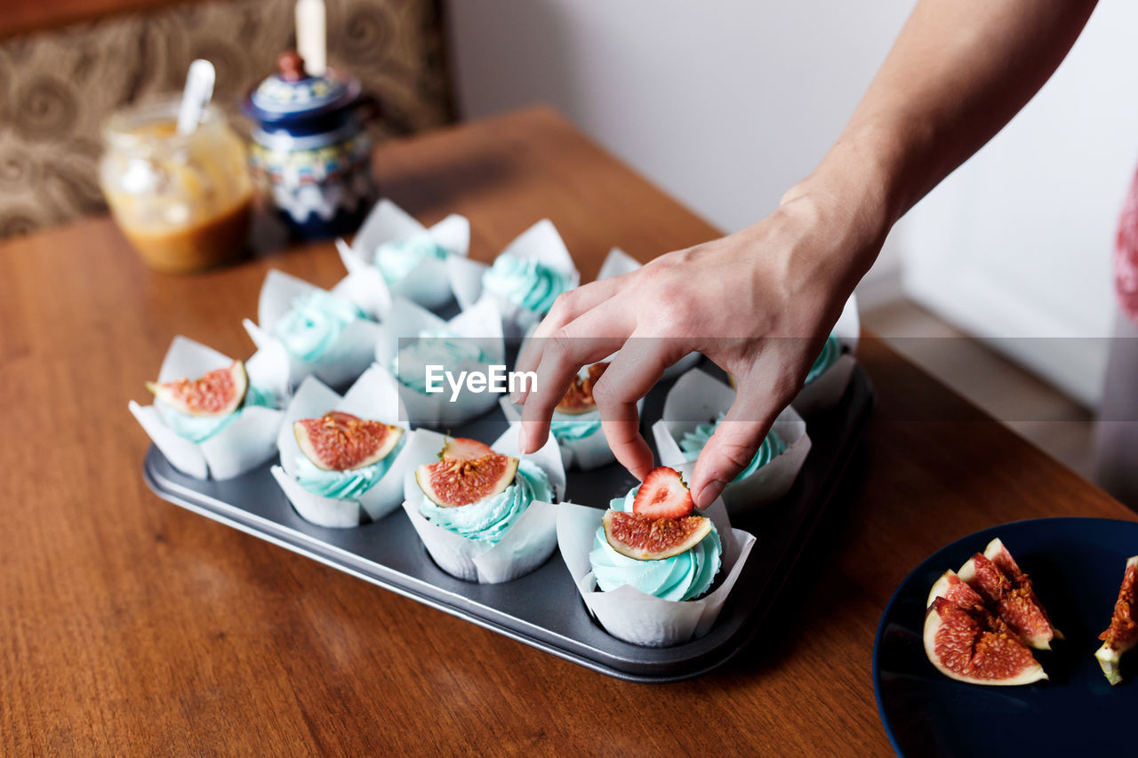 Decorating homemade chocolate muffins with blue cream topping and fig