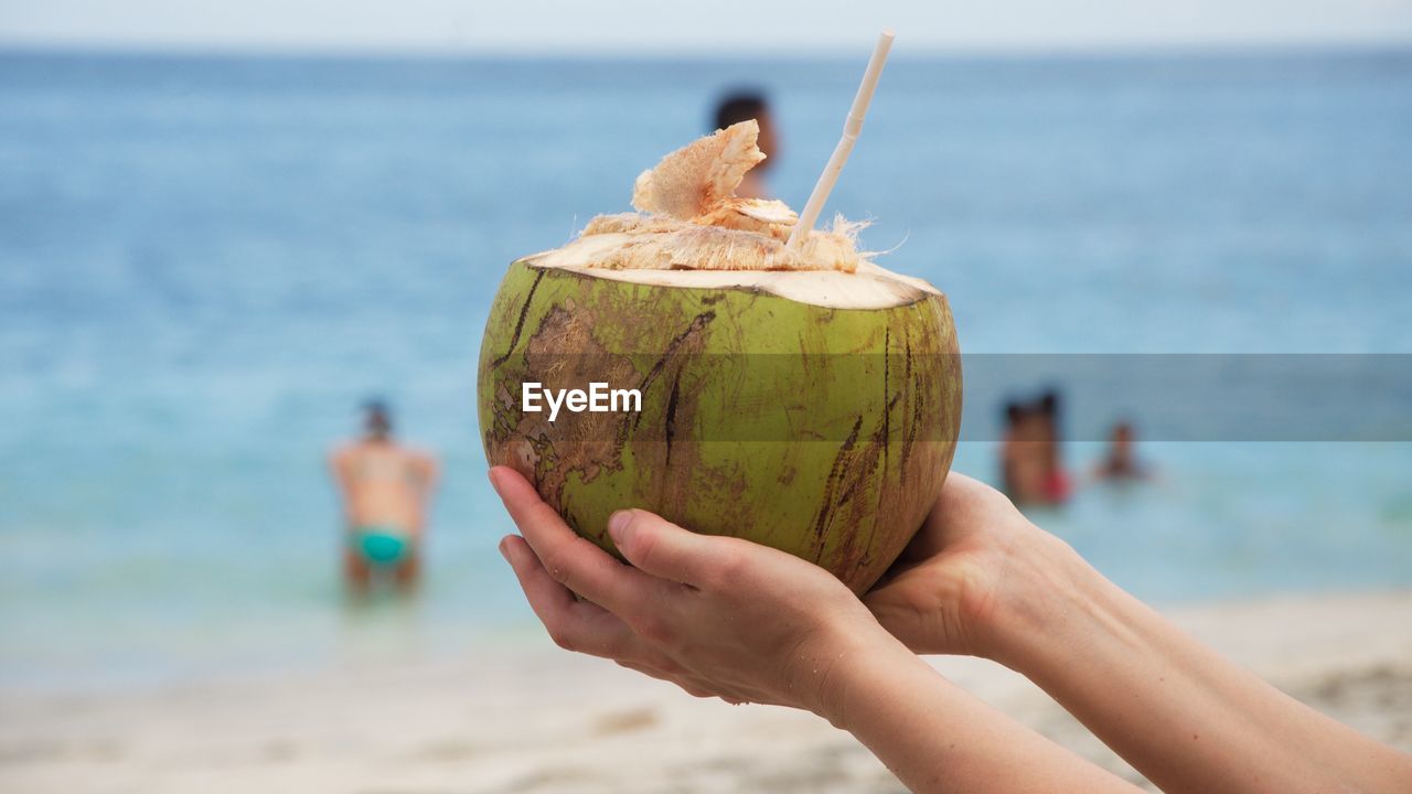 Cropped image of person holding coconut at beach