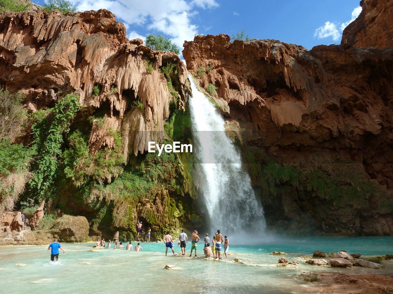 People on rock against waterfall and sky