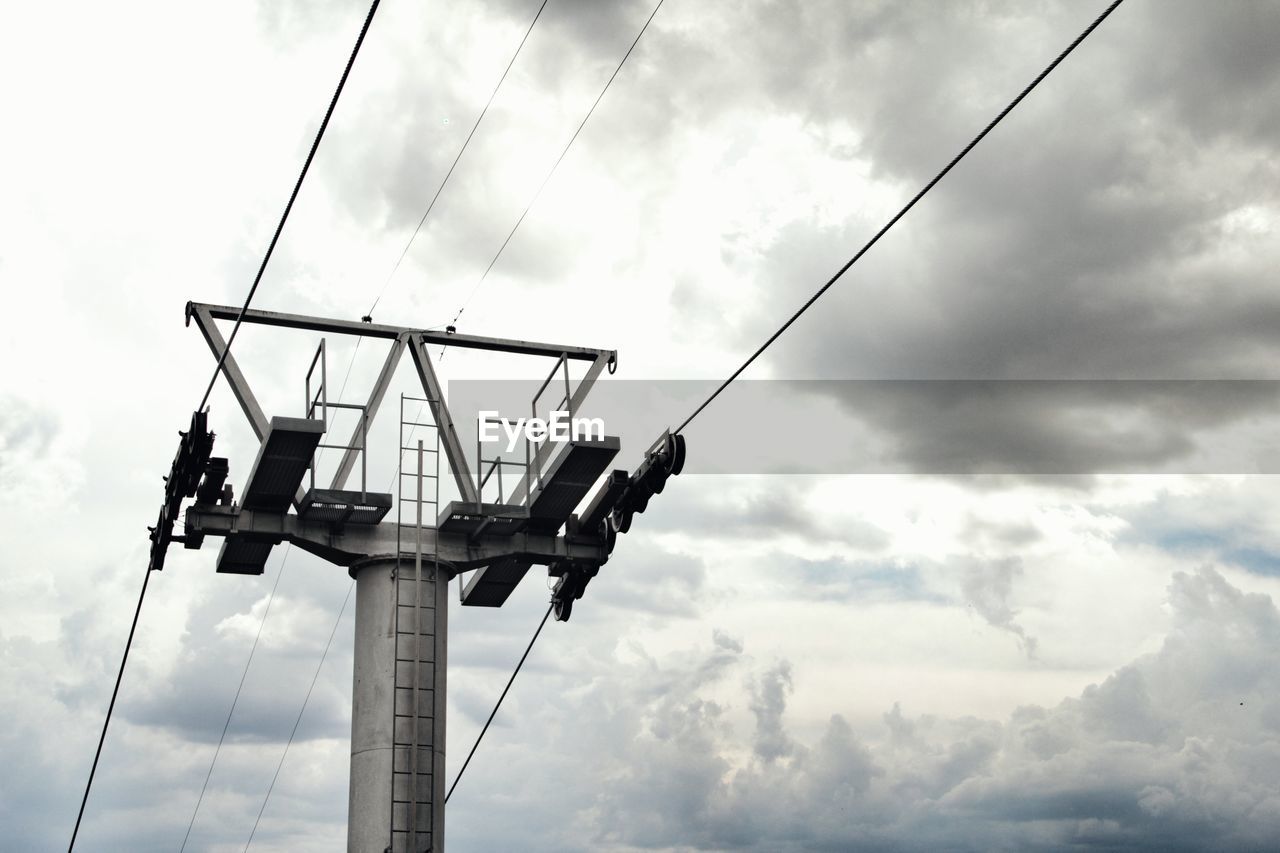 Low angle view of overhead cable car pole against cloudy sky