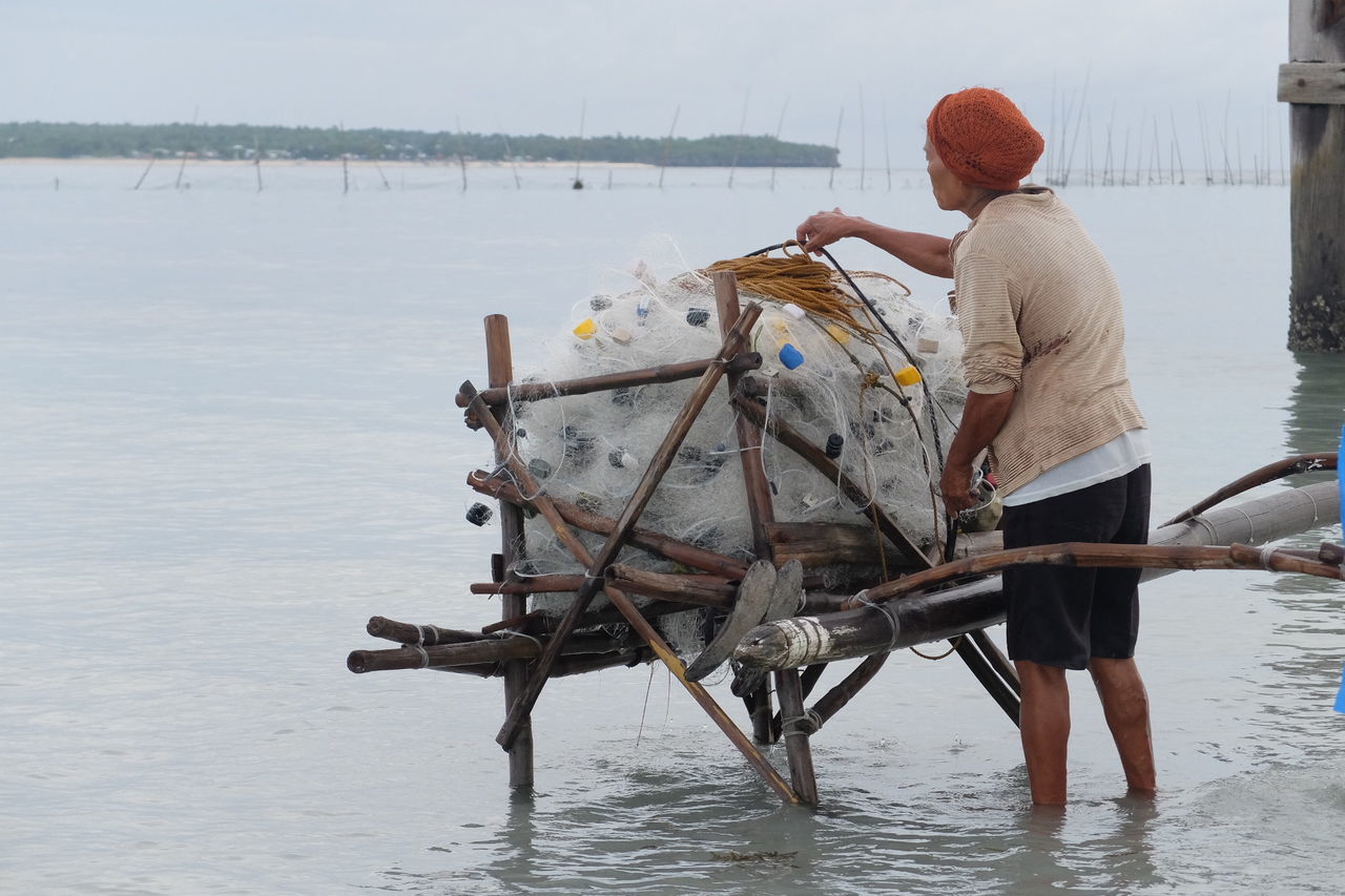 Rear view of woman tying fishing net in lake