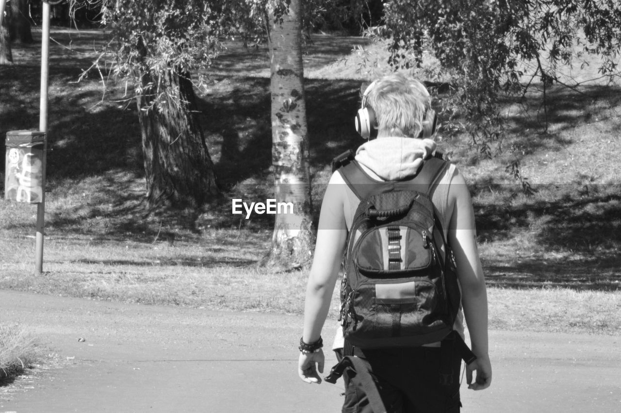 Rear view of backpack man walking on road during sunny day