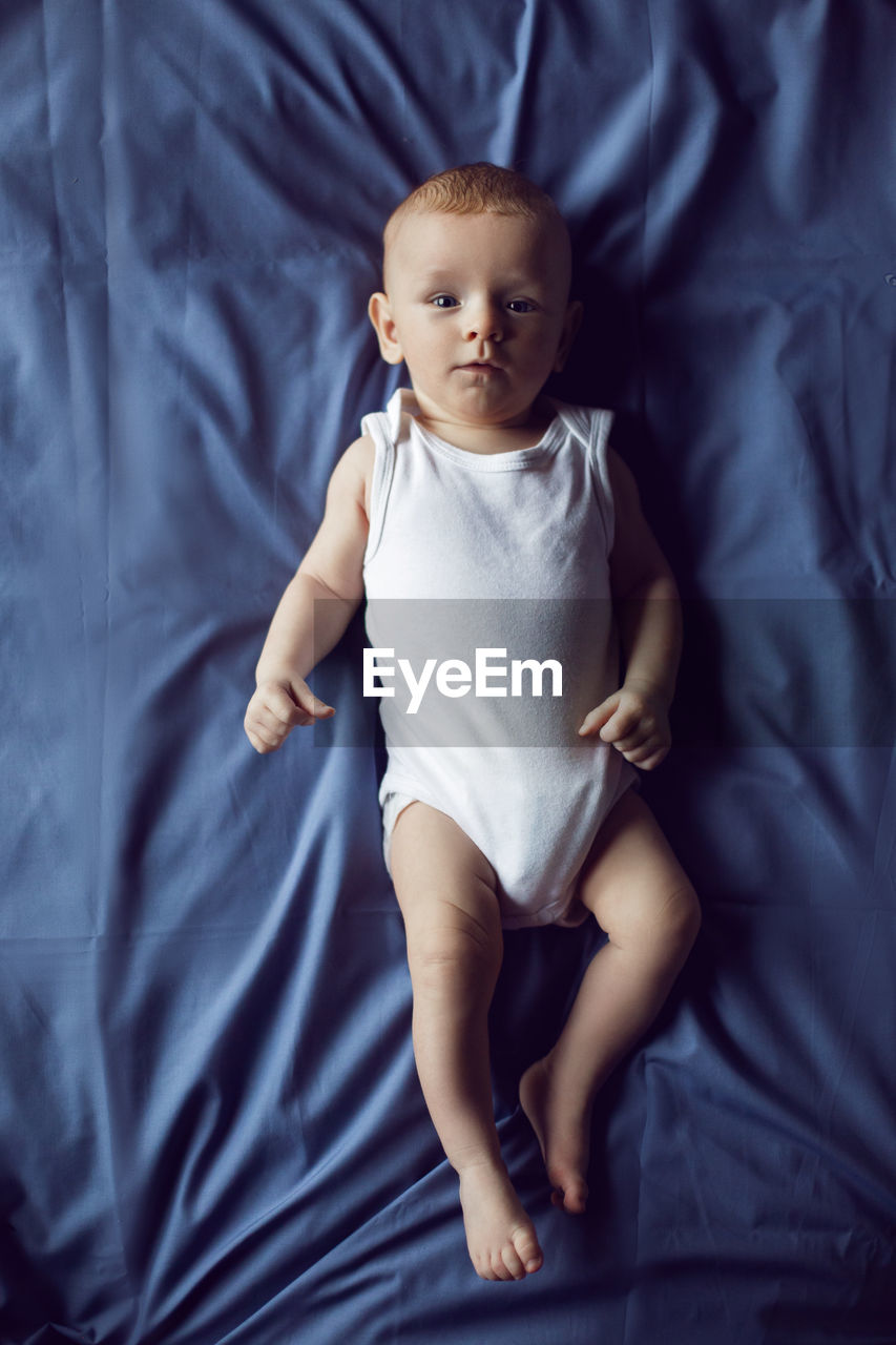 Baby boy blonde in white bodysuit lying on the bed