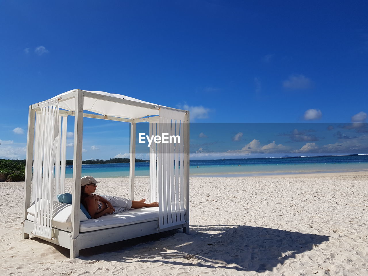 Full length of woman relaxing on four poster bed at beach during sunny day