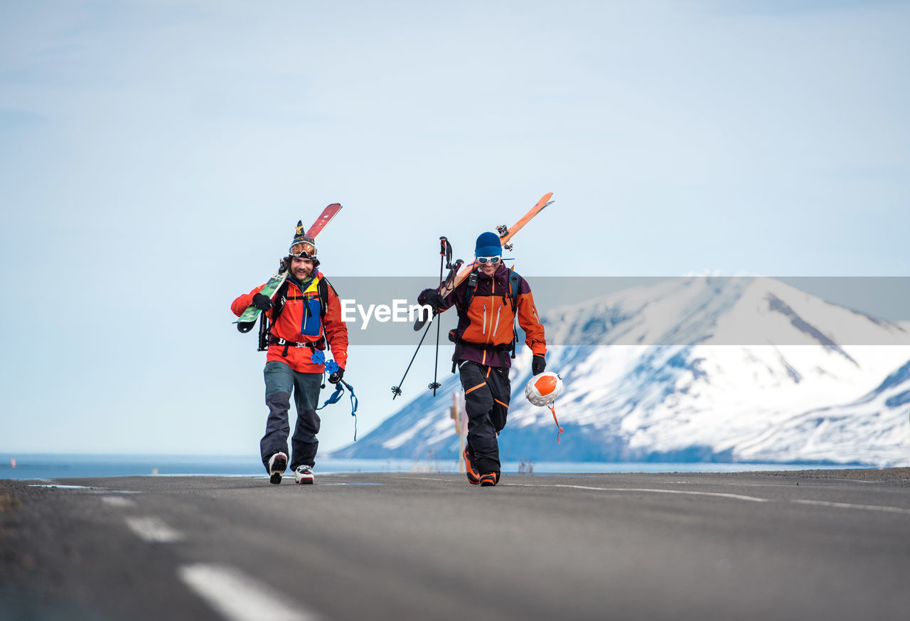 Two men walking with skis on a paved road in iceland with mountains