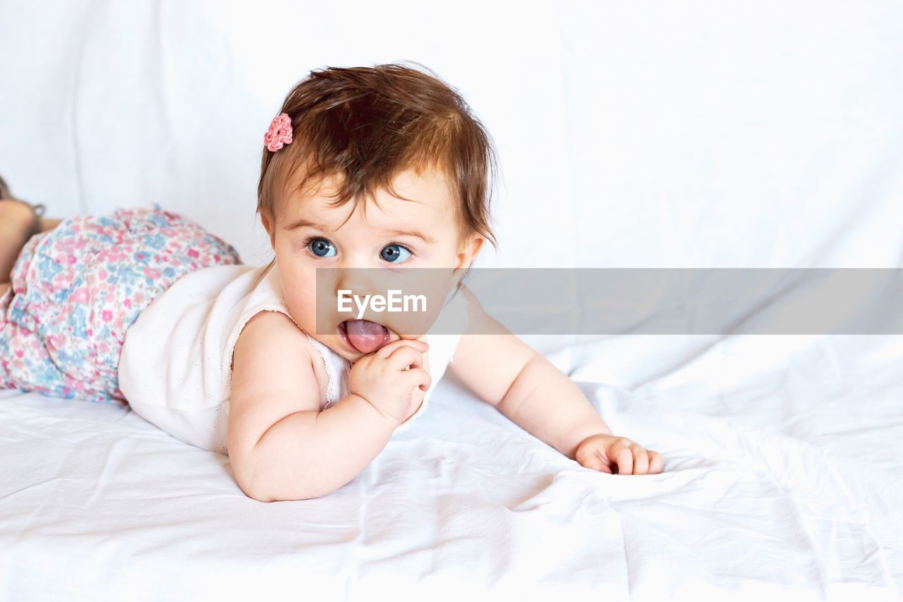 Cute baby girl looking away lying on bed at home