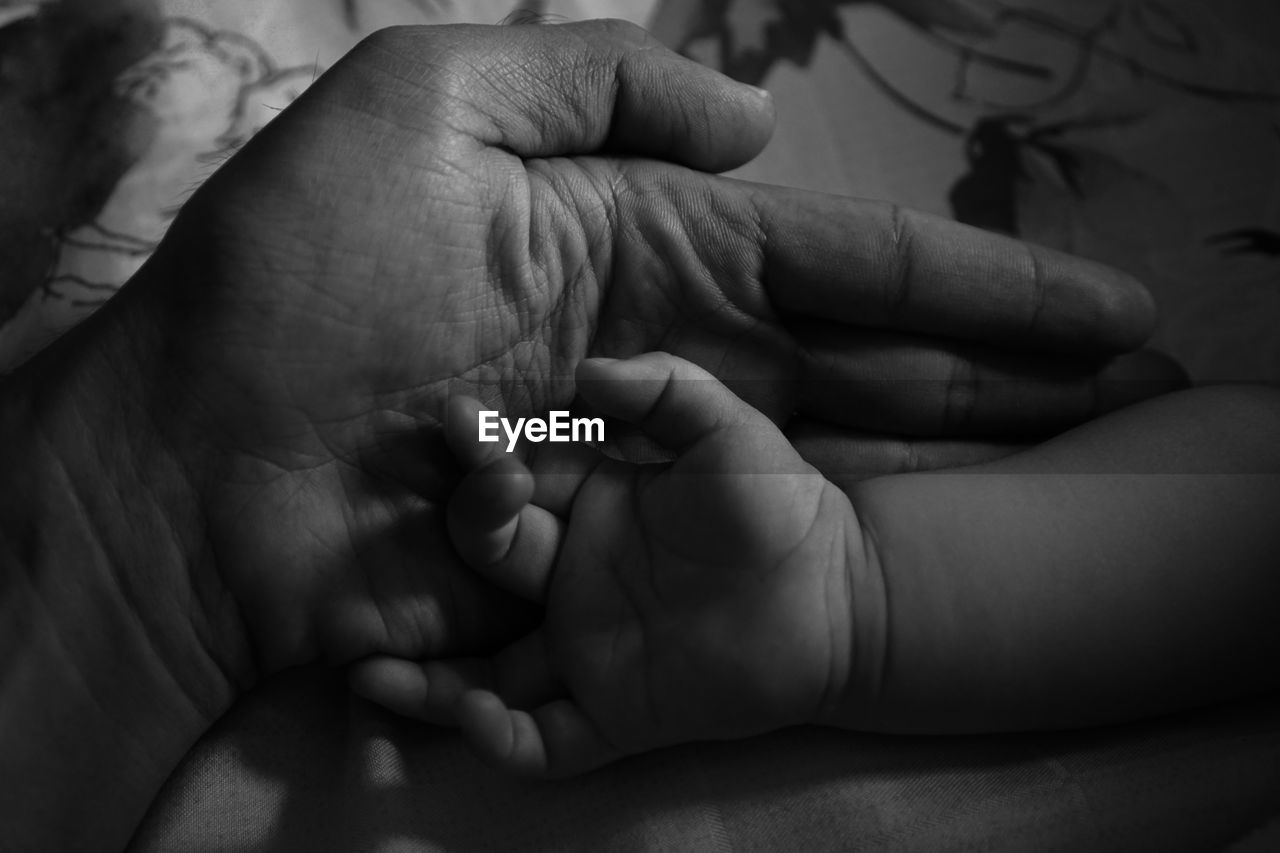 Cropped hands of parent and baby on bed at home