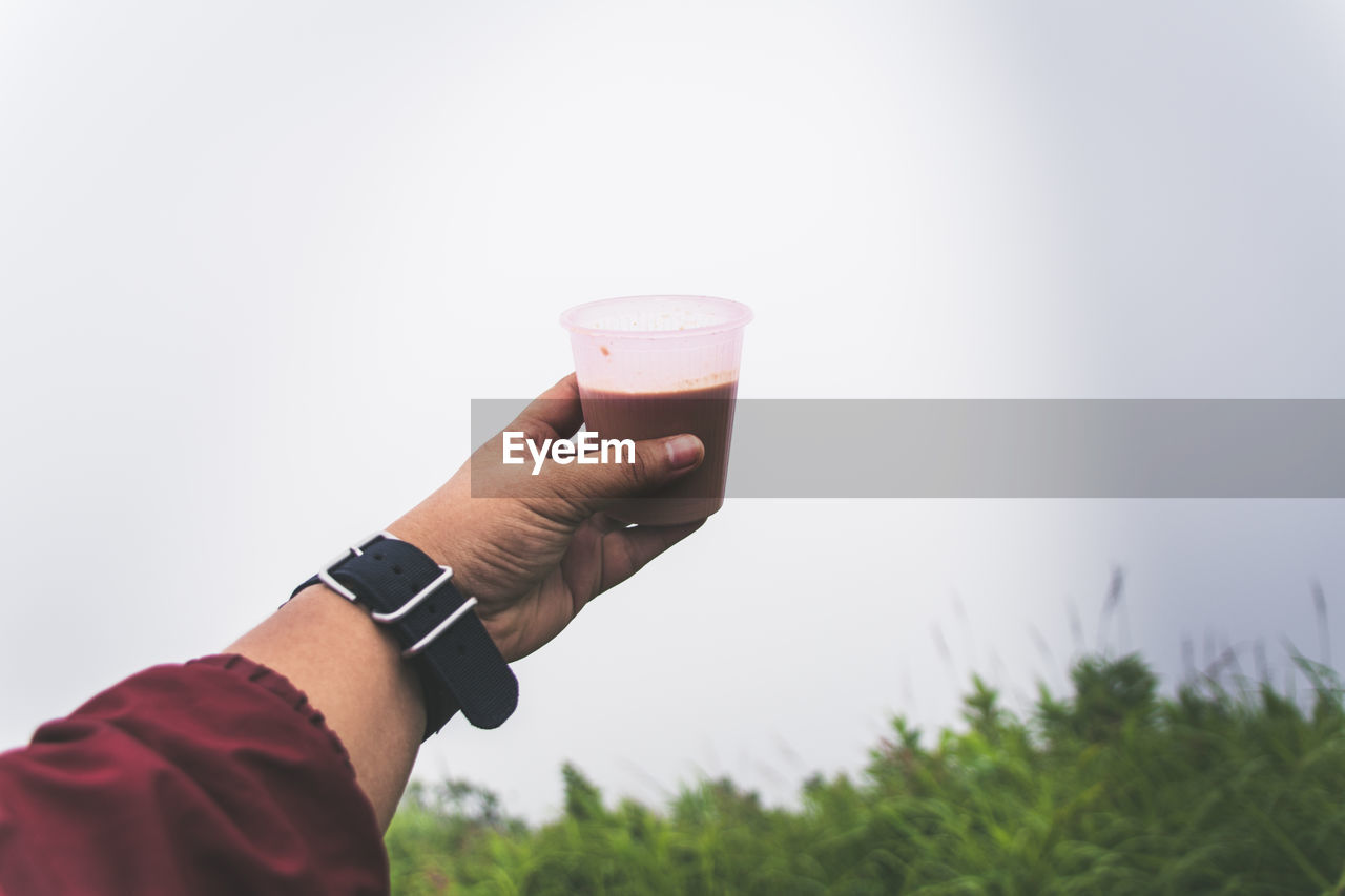 Cropped hand holding drink against clear sky