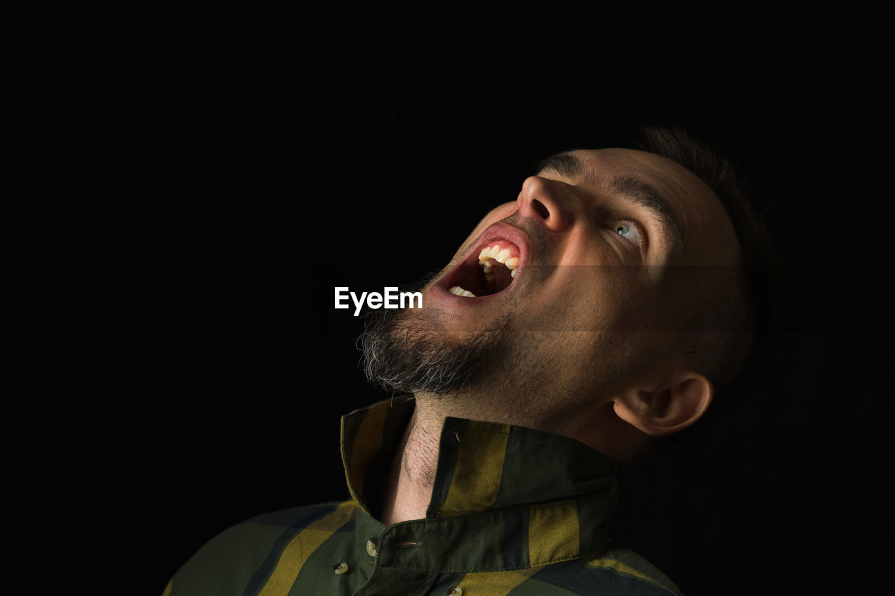 black background, one person, studio shot, headshot, portrait, mouth open, adult, copy space, indoors, men, darkness, beard, human mouth, facial hair, emotion, shouting, looking, performing arts, looking up, concert, young adult, entertainment, performance, anger