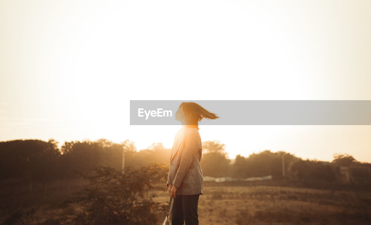 Rear view of woman standing against sky during sunset