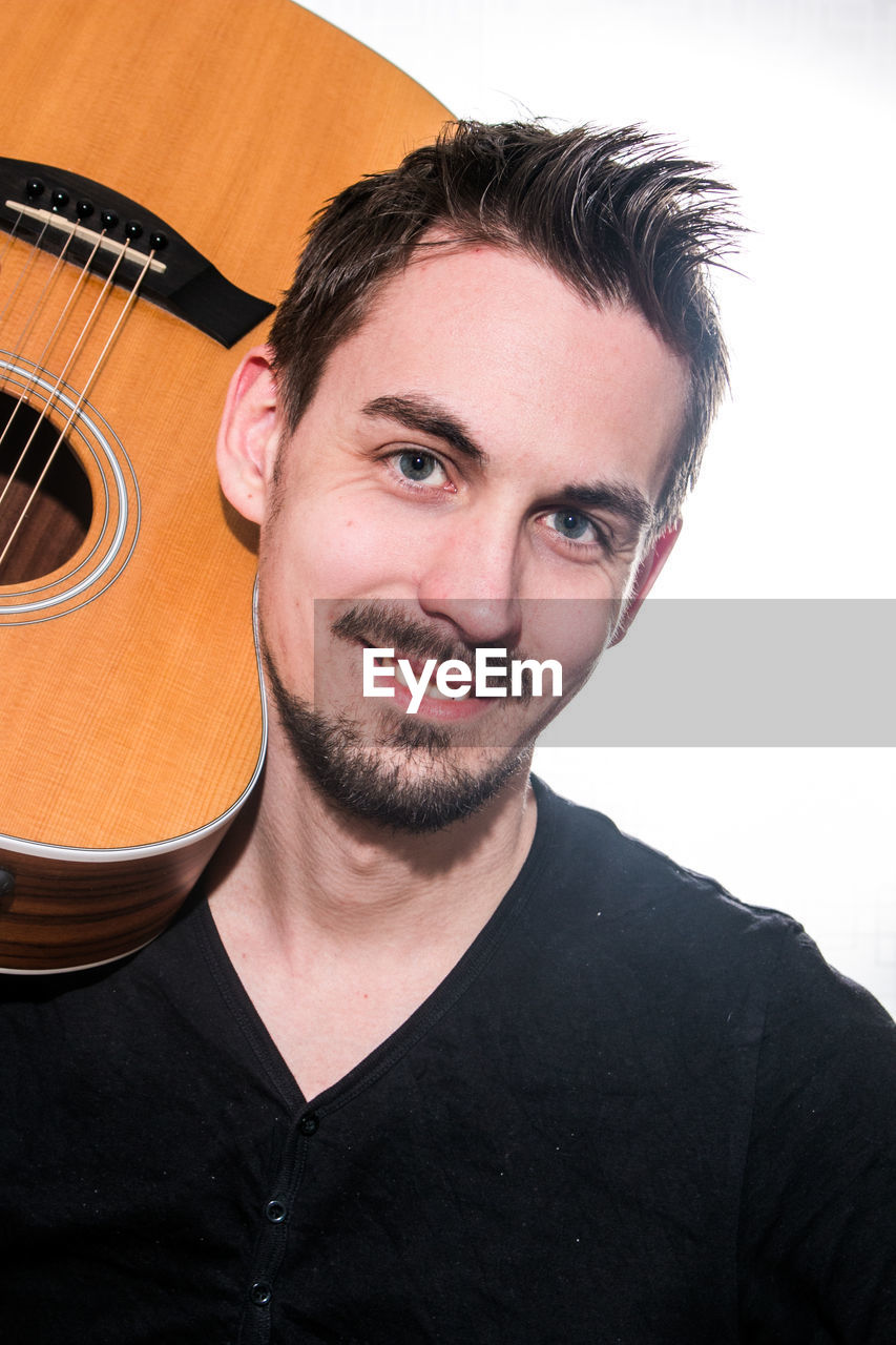Close-up portrait of man holding guitar against white background