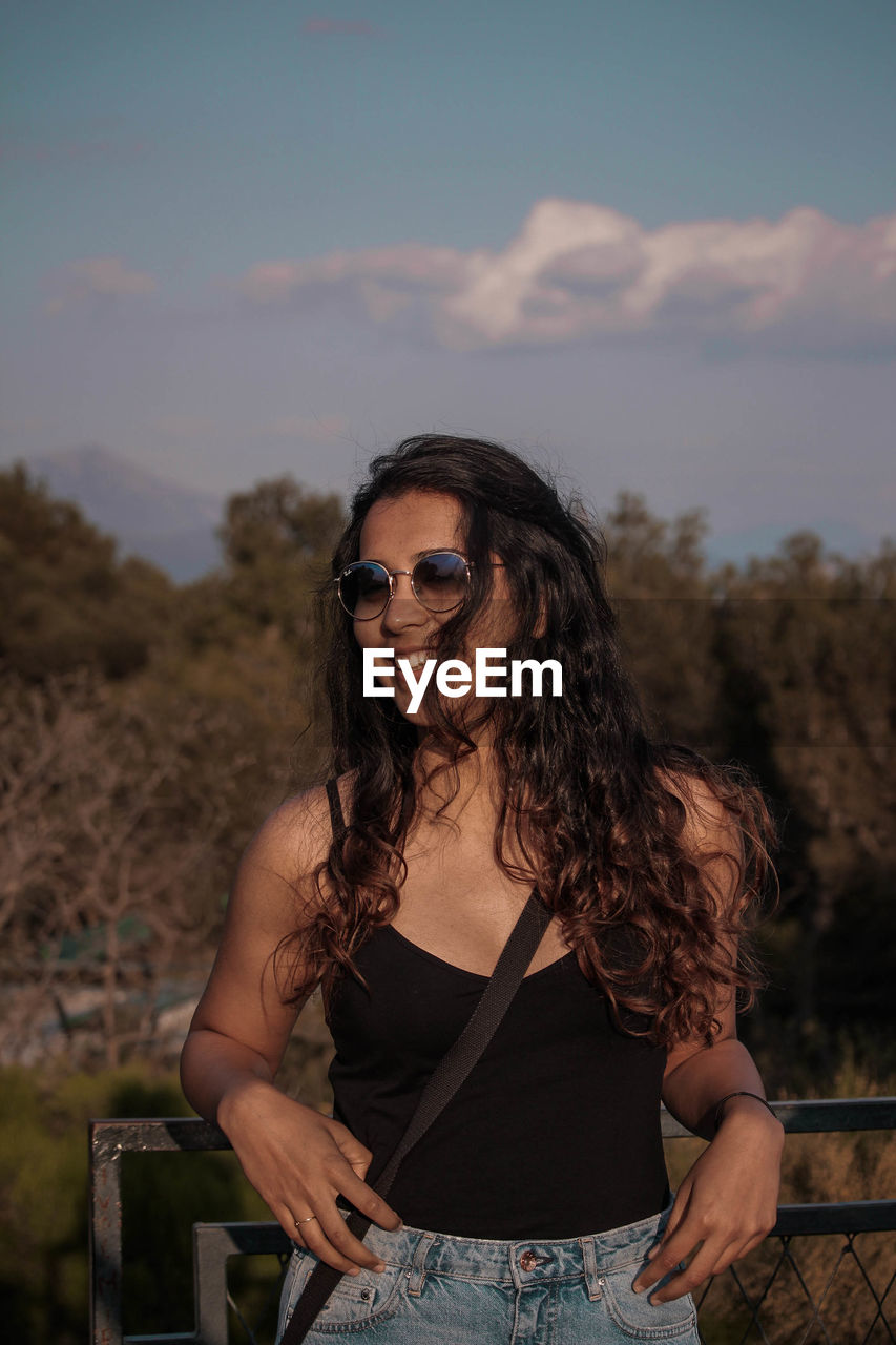 Smiling young woman wearing sunglasses against sky