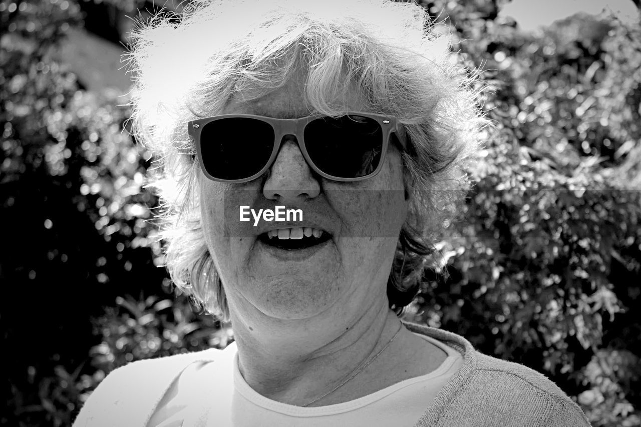 Portrait of mature woman wearing sunglasses against plants