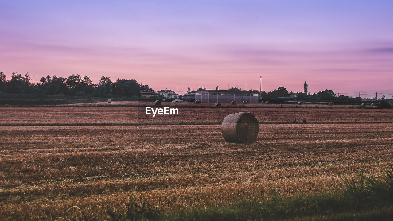 Hay bales on field against sky during sunset