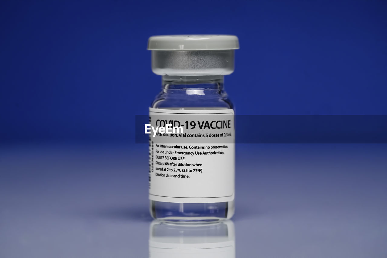 Medical glass vial with coronavirus vaccine placed against blue background