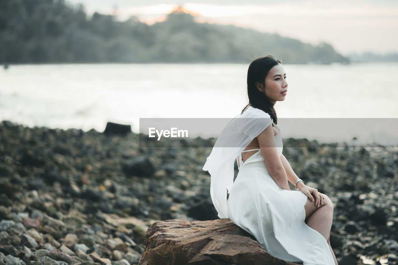 Side view of young woman sitting on rock at beach