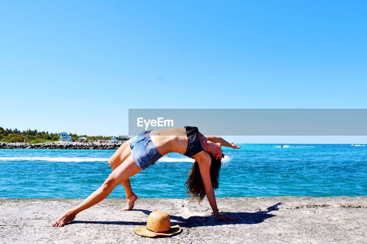 Full length of woman on beach against clear blue sky