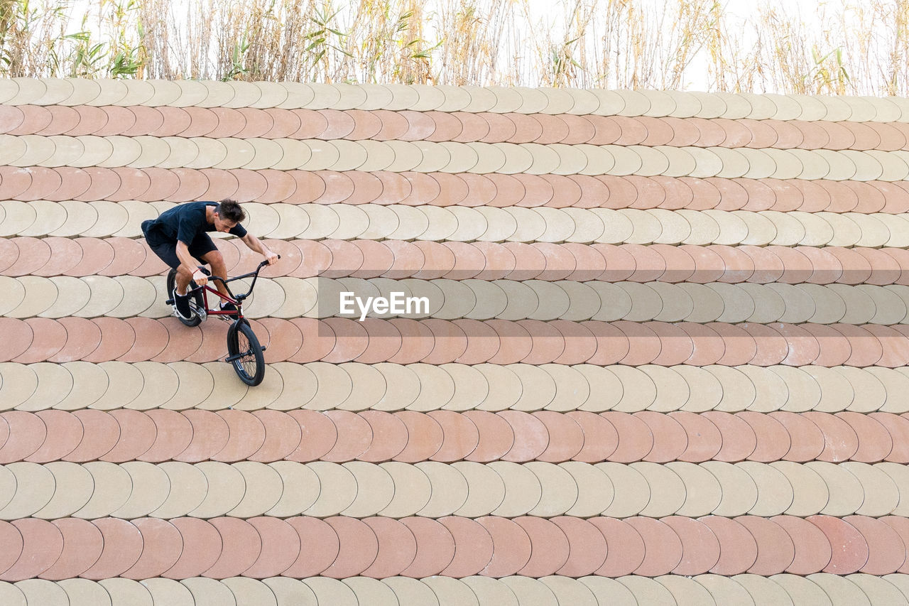 Full body man in casual clothes doing wallride trick on bmx bicycle on slope on summer weekend day in skate park