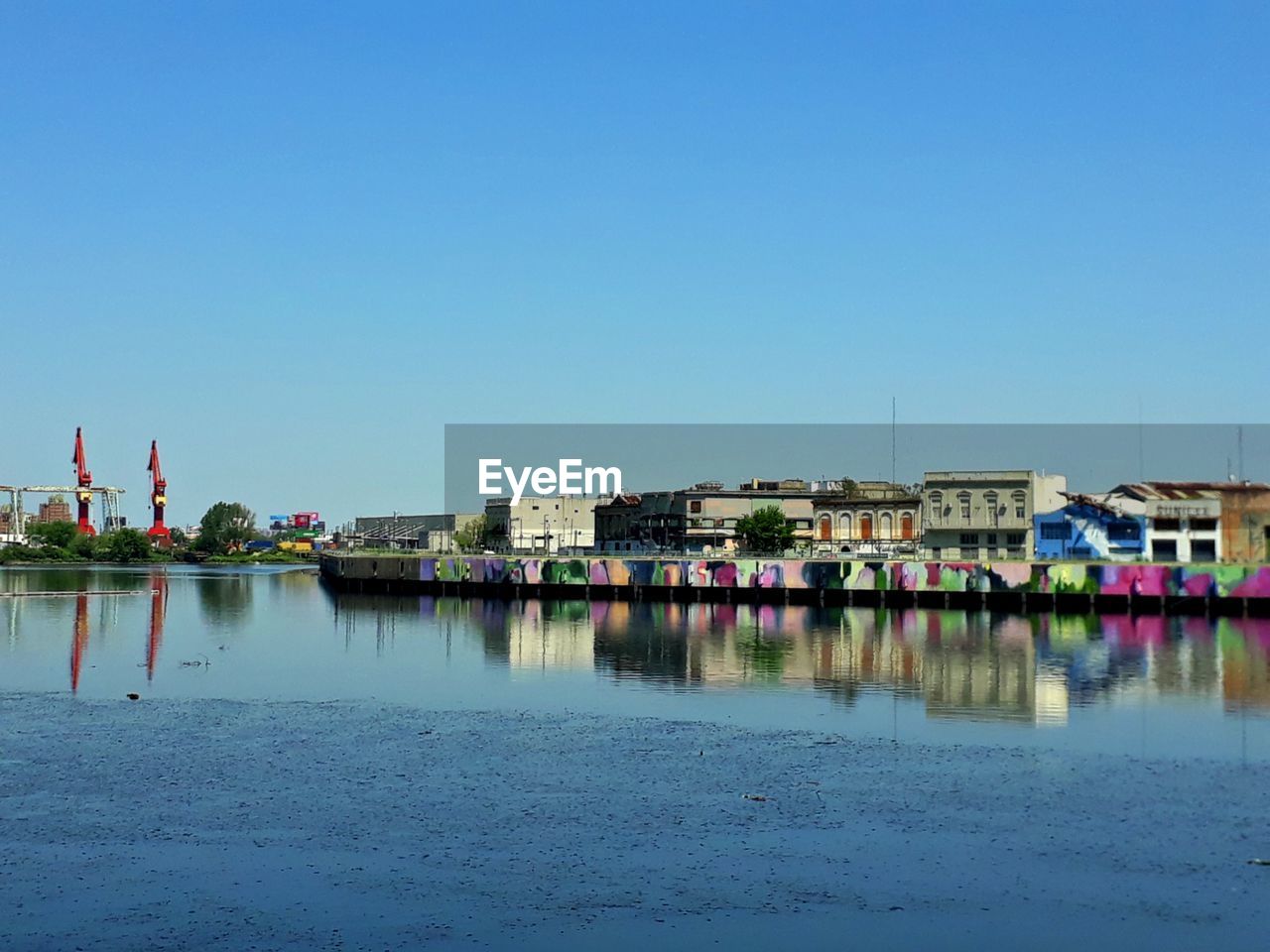 Buildings by lake against clear blue sky