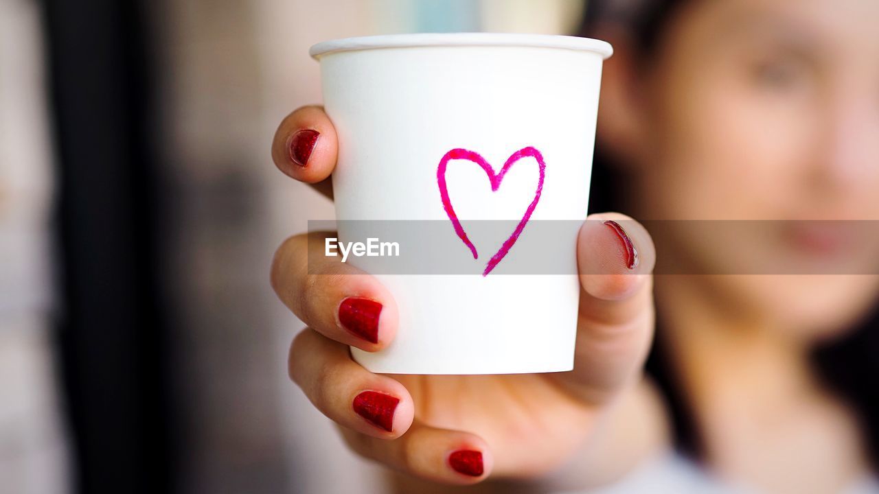 Close-up of woman holding disposable cup with heart shape drawn