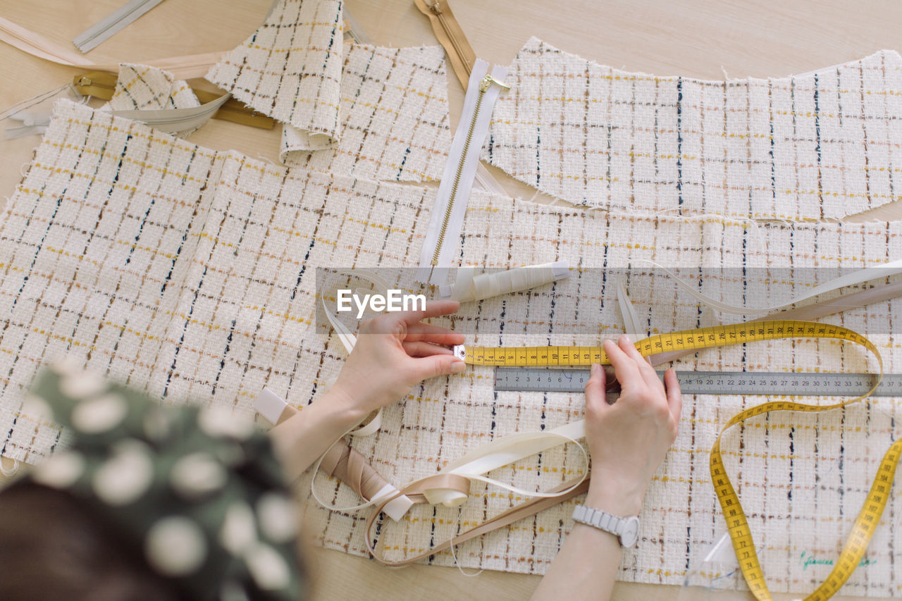 High angle view of woman measuring fabric with tape and ruler on table