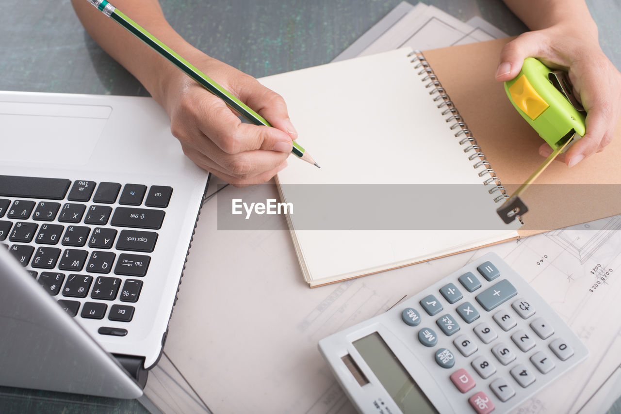 Cropped hands of woman writing on book at desk