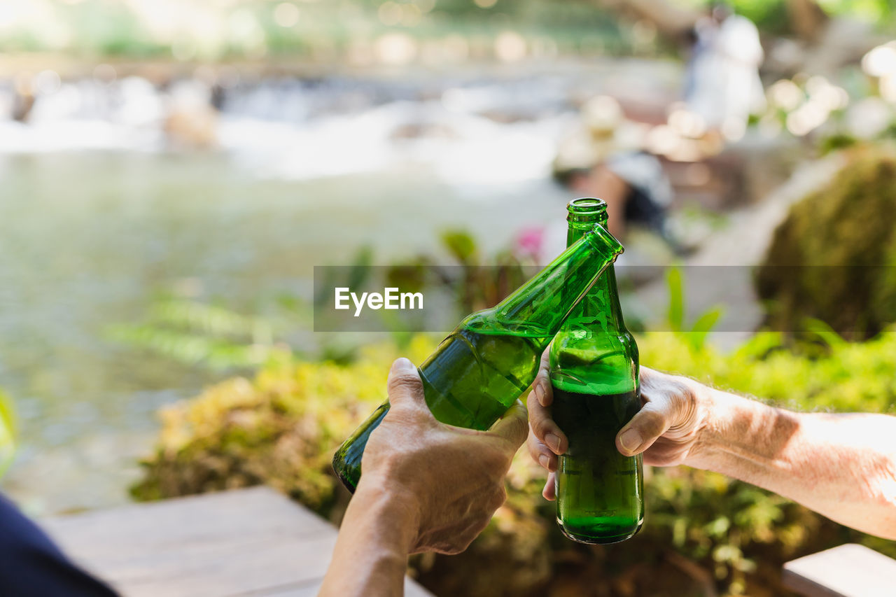 Senior man toasting with bottle beer together with his son on vacation.