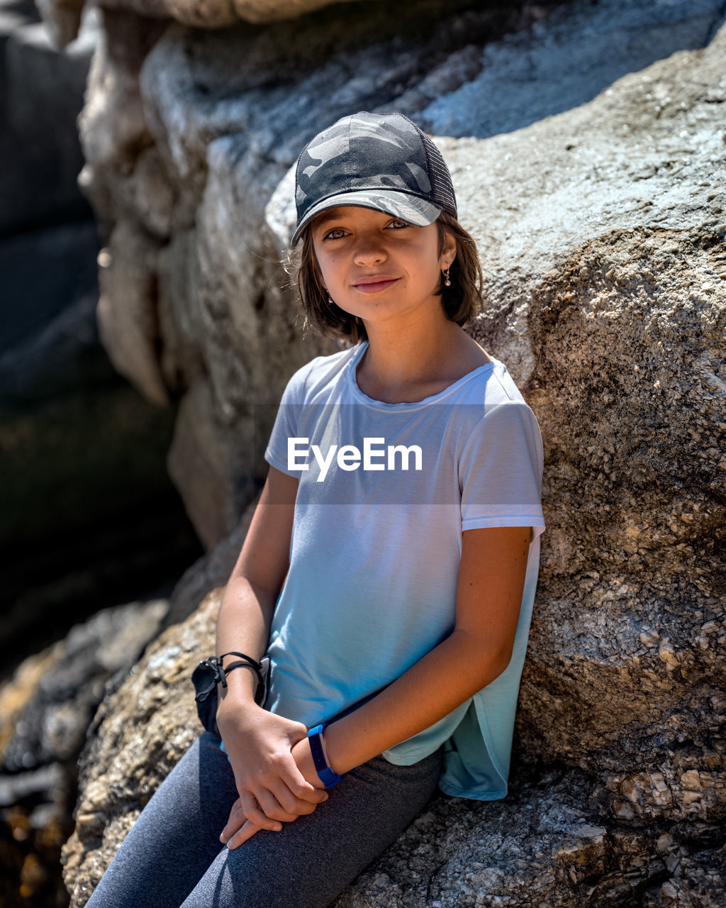 Portrait of cute girl wearing cap girl sitting on rock