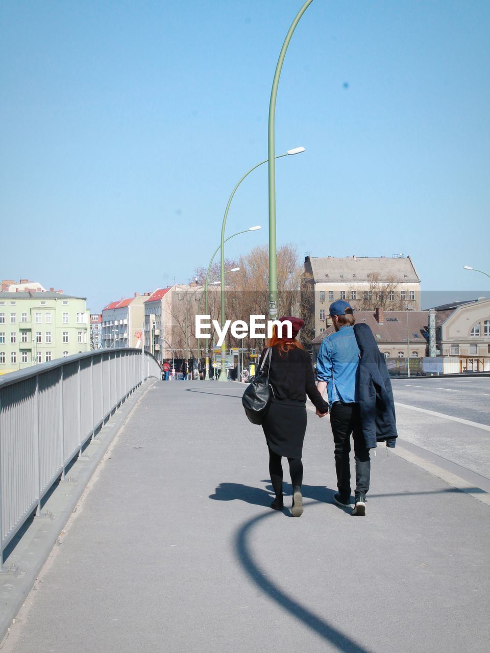 Full length rear view of couple walking on bridge against sky