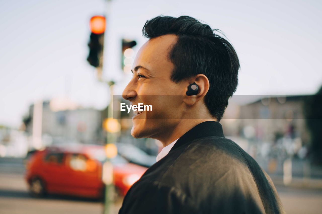Cheerful man looking away while wearing in-ear headphones in city