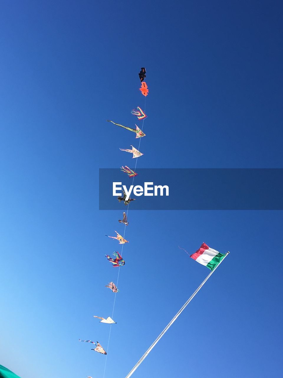 Low angle view of kites and italian flag against clear blue sky