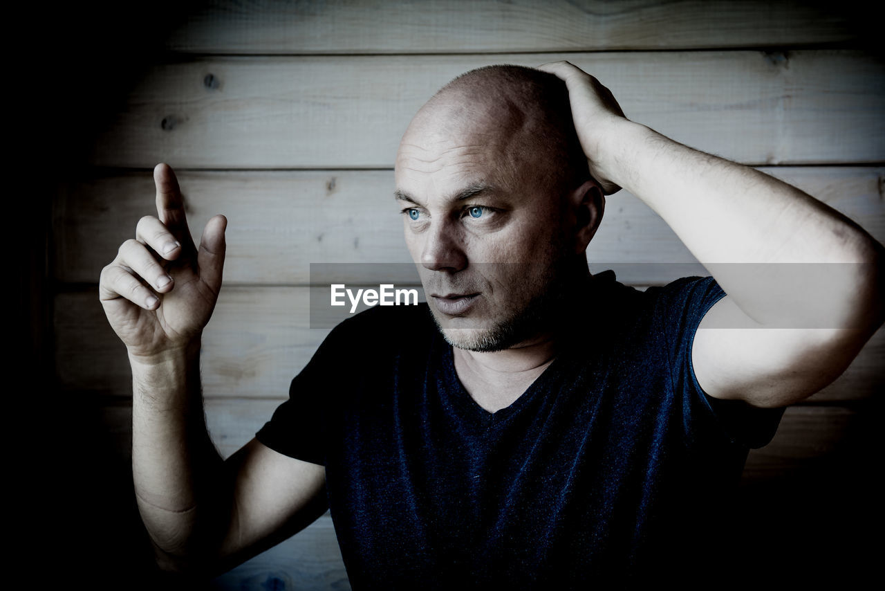 Man looking away while standing by wooden wall