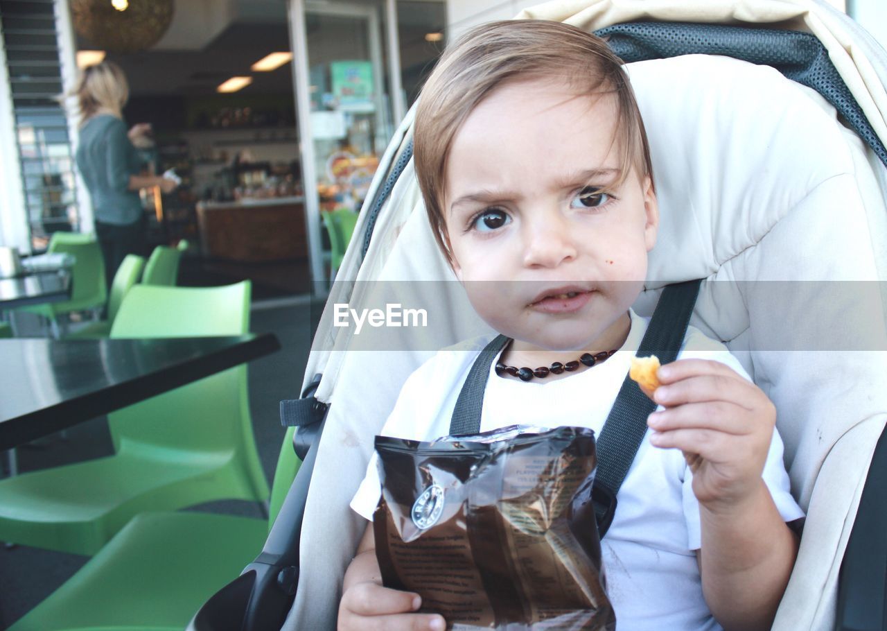 Little boy sitting in stroller eating potato chips