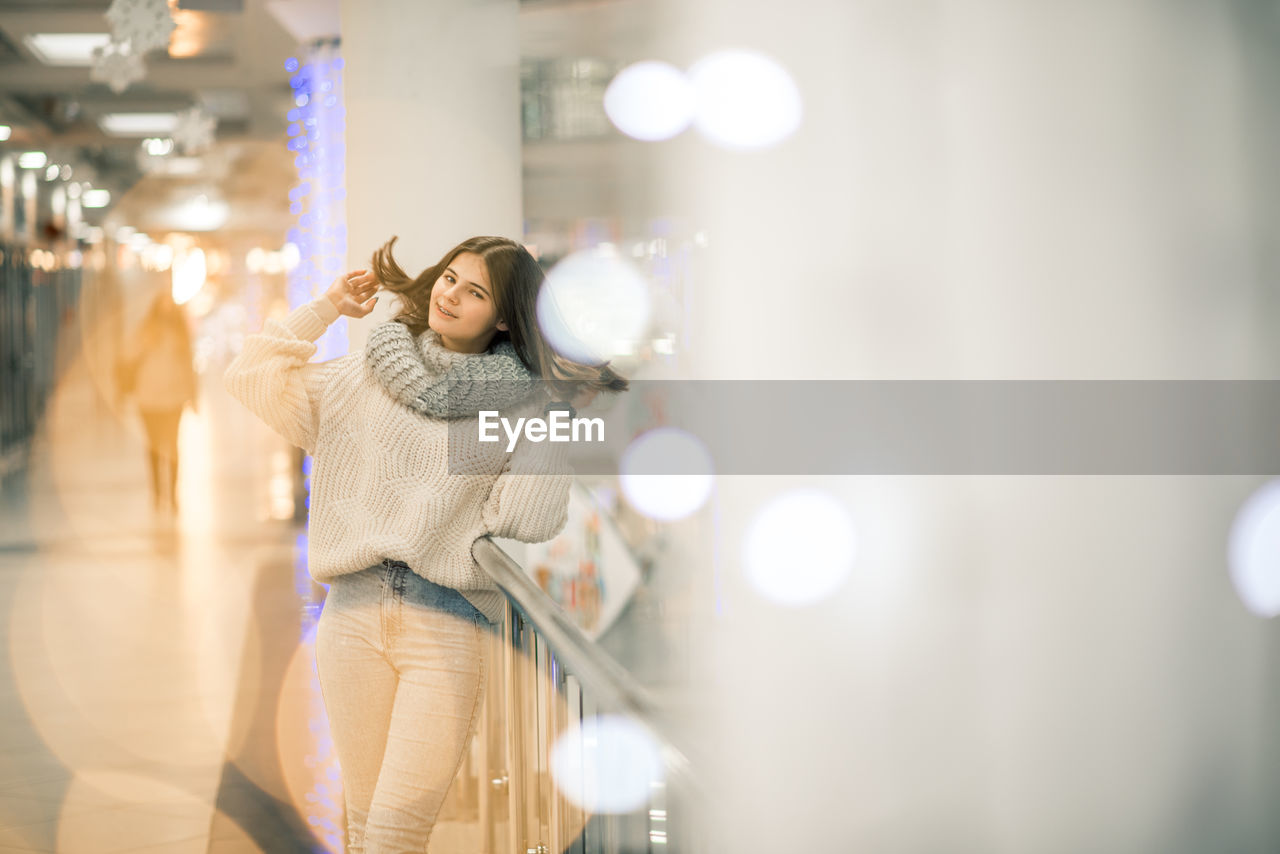 Portrait of smiling teenager girl standing by railing at shopping mall